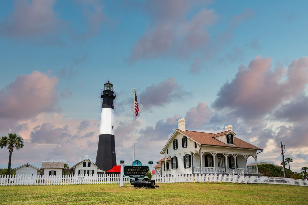 The iconic black and white Tybee Island Light Station under a dramatic evening sky, highlighting the historic regional day trips and sightseeing destinations easily accessible from Southern Charm Retreats.