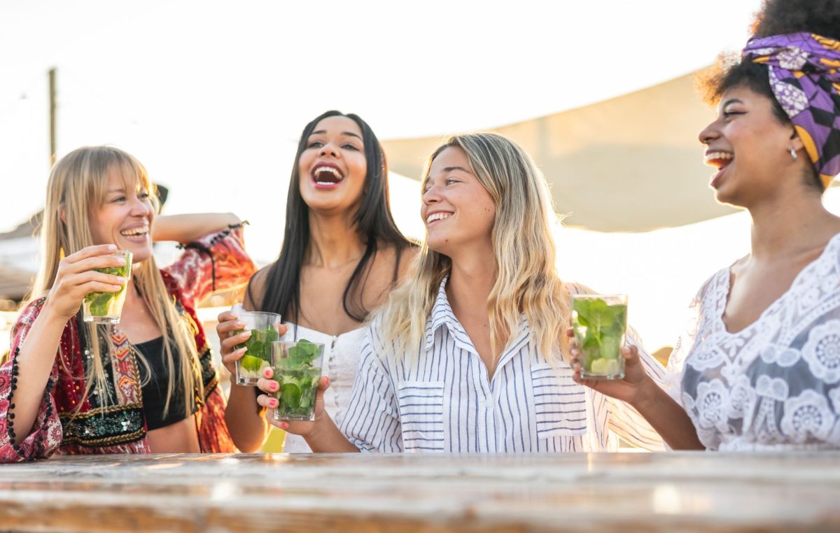 A group of smiling friends sharing laughs and raising glasses of fresh mint mojitos at an outdoor bar, showcasing the local breweries and waterfront dining scenes near Southern Charm Retreats.